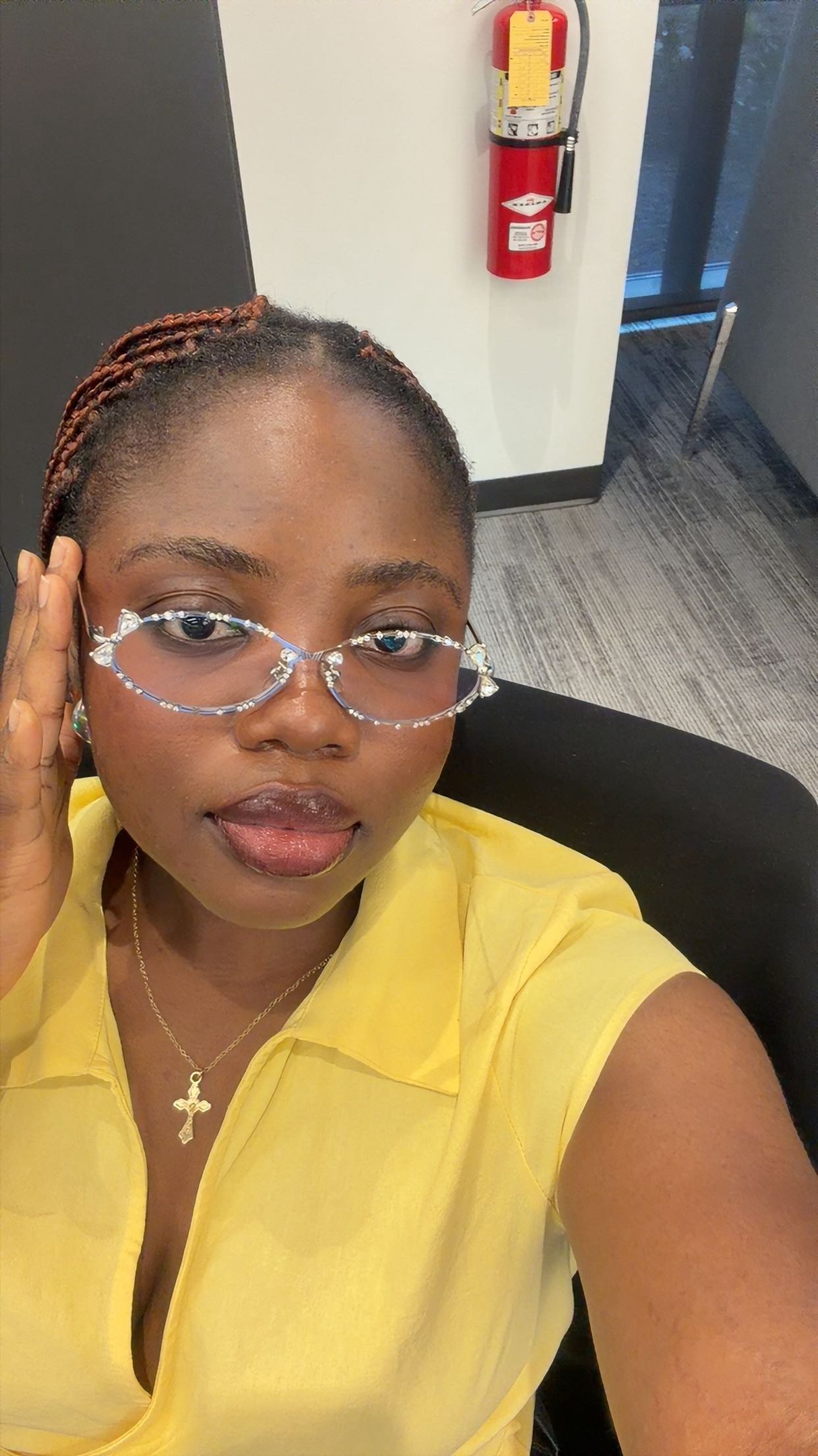 Photo of Dark Skin Woman with silver slim frame glasses with tiny embellishments, a dainty cross necklace. In a yellow shirt